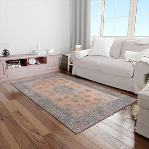 May include: Rectangular rug with a peach central field and a detailed border in blue and red. The rug has an intricate floral pattern. It's placed on a wooden floor in a living room setting. The rug measures approximately 200cm x 300cm.