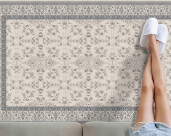 May include: A white rug with a grey floral pattern and a grey border. The rug is on a light grey surface.