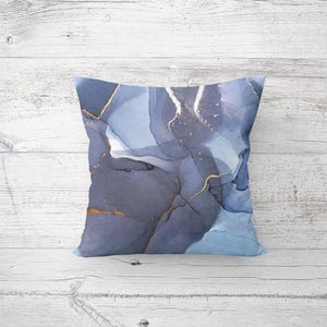 May include: A decorative throw pillow with a blue and gold abstract design. The pillow features a marbled pattern with shades of blue and gold accents.