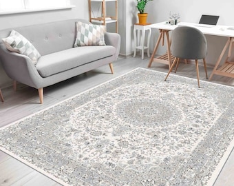 May include: A white and grey patterned area rug with a floral design. The rug is in a living room setting with a grey sofa and a wooden desk with a chair.