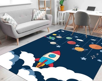 May include: A rectangular rug with a dark blue background featuring a cartoon rocket ship blasting off through white clouds. Planets and stars are suspended from above. The rug is designed for a child's room.