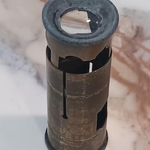May include: A vintage brass and steel magnifying glass with a dark gray rim around the lens. The cylindrical body has cut-out sections and a dark gray base. The magnifying glass is designed to magnify small objects.