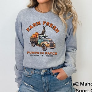 May include: Sport grey sweatshirt with a graphic of a vintage truck filled with pumpkins and a dog. The text reads "Farm Fresh Pumpkin Patch Locally Grown Hand-Picked". The sweatshirt is a light grey color.
