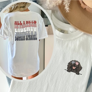 May include: White t-shirt with the text "All I need is freedom, liberty, justice & a Boykin Spaniel" printed on the back. A second white t-shirt features a cartoon Boykin Spaniel wearing sunglasses with red, white, and blue accents.