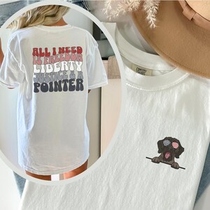 May include: White t-shirt with a graphic on the back that says "All I need is freedom, liberty, justice & a pointer". The front of the shirt has a small graphic of a brown dog wearing sunglasses with an American flag design.