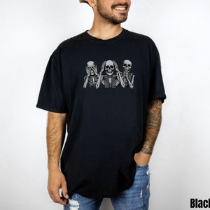 K&ouml;nnte beinhalten: Schwarzes T-Shirt mit einer Grafik von drei Skeletten in der Pose "Nichts sehen, nichts h&ouml;ren, nichts sagen". Die Skelette sind hellgrau. Das Wort "Black" ist unten rechts aufgedruckt.
