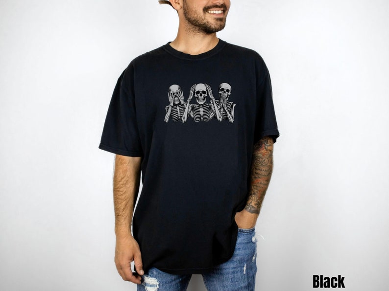 K&ouml;nnte beinhalten: Schwarzes T-Shirt mit einer Grafik von drei Skeletten in der Pose "Nichts sehen, nichts h&ouml;ren, nichts sagen". Die Skelette sind hellgrau. Das Wort "Black" ist unten rechts aufgedruckt.