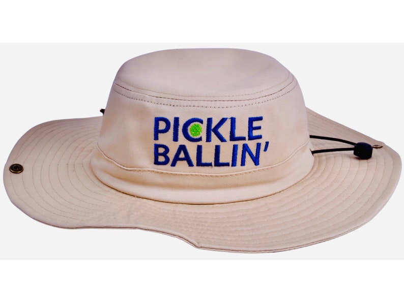 May include: A beige sun hat with a blue and green embroidered logo that says "PICKLE BALLIN'" on the front.