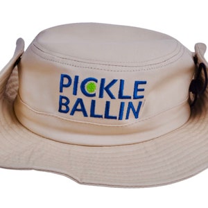 May include: A tan, wide-brimmed sun hat with a blue and green embroidered logo that says "PICKLE BALLIN".