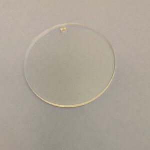 May include: A clear, circular acrylic blank with a small hole at the top for hanging. The disc is transparent and has a smooth surface. Ideal for crafting projects, ornaments, or personalized gifts.