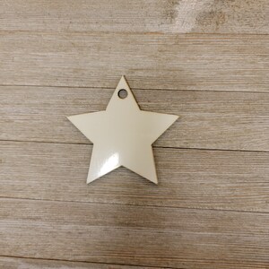 May include: A white wooden star ornament with a hole at the top for hanging. The star is on a light brown wooden background.