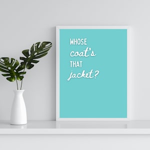 May include: A white framed print with a light blue background and the text "Whose coat's that jacket?" in white cursive font. A green plant in a white vase is on a white shelf below the print.