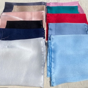May include: A stack of ten fabric swatches in various colors, including white, light blue, navy blue, black, red, teal, pink, beige, and gray. The swatches are arranged in a vertical stack, with the white swatch at the bottom and the gray swatch at the top.