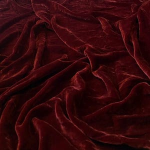 May include: A close-up of a deep red velvet fabric with soft, flowing folds. The fabric has a luxurious and elegant appearance.