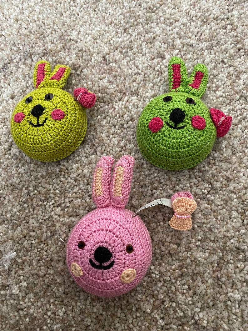 Puede incluir: Tres cintas m&eacute;tricas de crochet con forma de conejo. Una es verde con detalles rosas, otra es rosa con detalles marrones y la &uacute;ltima es verde con detalles rojos.