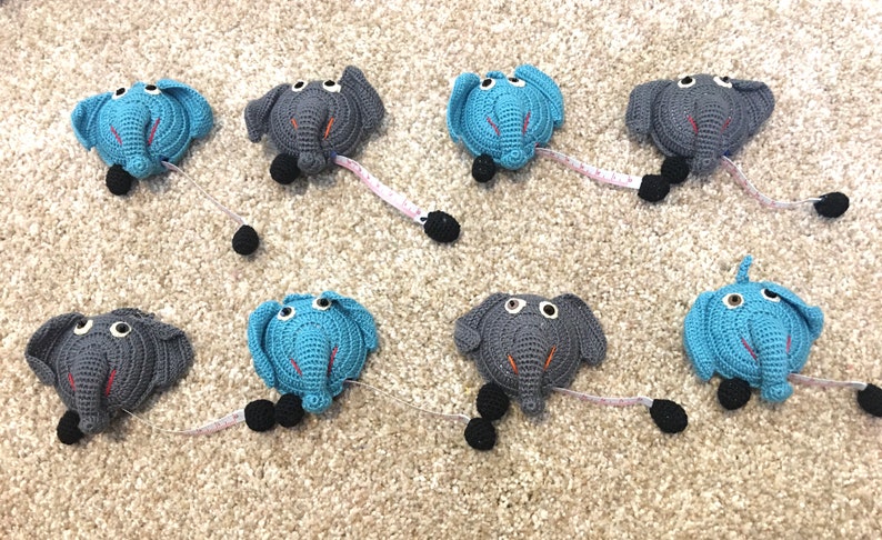 Puede incluir: Ocho cintas m&eacute;tricas de crochet con forma de elefante. Cuatro son grises con detalles naranjas y cuatro son azules con detalles naranjas. Cada elefante tiene ojos negros y un pomp&oacute;n negro en el extremo de la cinta m&eacute;trica.