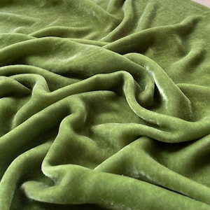 May include: A close-up of a soft, green velvet fabric. The fabric is smooth and has a subtle sheen.