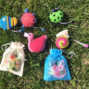 Puede incluir: Un conjunto de cintas m&eacute;tricas de crochet con forma de varios animales, incluyendo una tortuga, una mariquita, un pez, un flamenco y un caracol. Las cintas se muestran sobre un lecho de hierba verde.