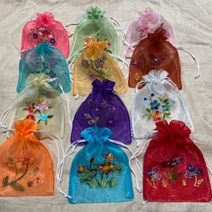 May include: Assortment of 10 small, colorful, sheer drawstring bags with embroidered floral designs. The bags are made of a delicate, translucent fabric and have a gathered top with a drawstring closure.