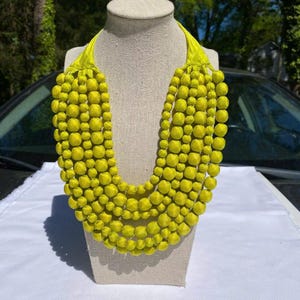 May include: A lime green multi-strand beaded necklace with a knotted closure. The necklace is made of large, round beads and is displayed on a mannequin.