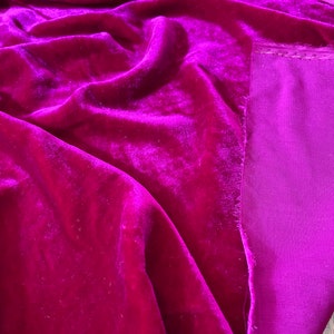 May include: A close-up of a deep magenta velvet fabric with a contrasting magenta lining. The fabric is soft and luxurious, with a subtle sheen.