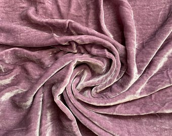 May include: A close-up of a soft, mauve velvet fabric with a subtle sheen. The fabric is draped and folded, showcasing its texture and drape.