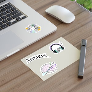 Puede incluir: Cuatro pegatinas en una superficie beige. Las pegatinas son: un CD plateado con estrellas y corazones, unos auriculares con el texto "Fake Shit", la palabra "Anxiety" y un cerebro con el texto "My mind is spinning out of control now".