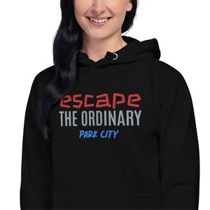Op de afbeelding: Zwarte hoodie met de tekst "escape the ordinary" in rode en grijze letters en "Park City" in blauwe letters.