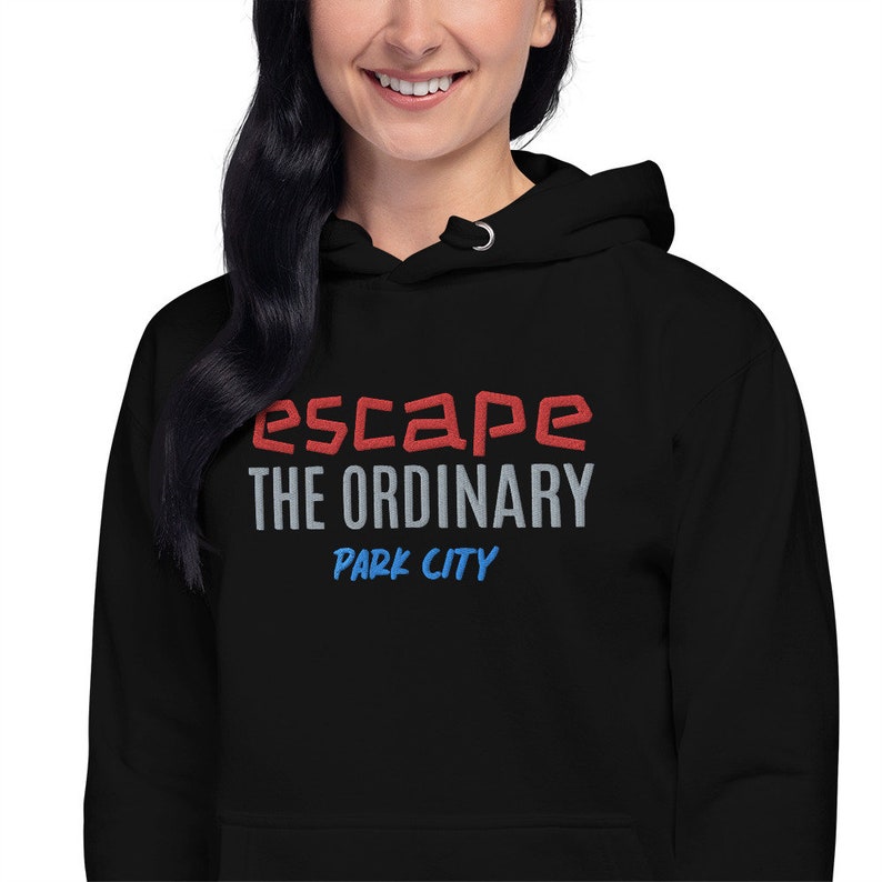 Op de afbeelding: Zwarte hoodie met de tekst "escape the ordinary" in rode en grijze letters en "Park City" in blauwe letters.