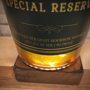 May include: A dark green bottle of Kentucky Straight Bourbon Whiskey, labelled "Special Reserve." The label indicates 45% alcohol by volume and 90 proof. The bottle rests on a small, square wooden coaster.