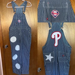 May include: Blue and white striped overalls with baseball-themed patches. Features a Phillies logo on the chest and a large "P" on the back. Includes a white star patch and baseball patches on the legs.