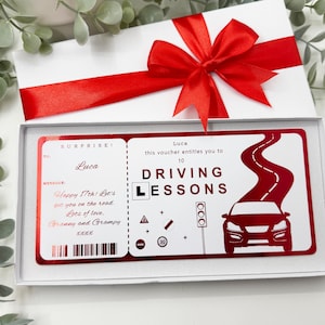 May include: A white gift box with a red ribbon containing a rectangular voucher for 10 driving lessons. The voucher features red text, a car graphic, a winding road, and traffic signs. It is addressed to Luca for a 17th birthday from Granny and Grampy.