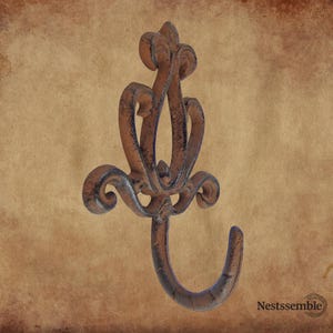 May include: Ornate, cast iron wall hook with a fleur-de-lis design. The hook is finished in a rustic brown with dark accents, featuring decorative swirls and a curved hook for hanging items. A decorative accent for any room.