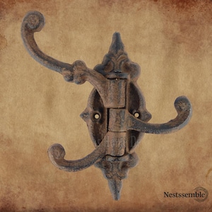 May include: Ornate, cast iron wall hook with three curved arms. The hook has a distressed, rustic finish with shades of brown and blue. The design features decorative flourishes and a hinged central section.