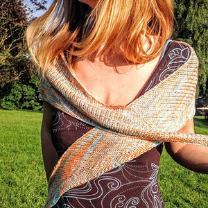 May include: A light brown, blue, and orange knitted shawl with a textured pattern. The shawl is draped over a person's shoulders and is tied at the front.
