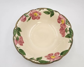 May include: A round ceramic bowl with a scalloped edge and a cream-colored interior. The rim is decorated with a hand-painted pattern of pink flowers with yellow centers and green leaves. The bowl features a brown painted trim along the scalloped edge.