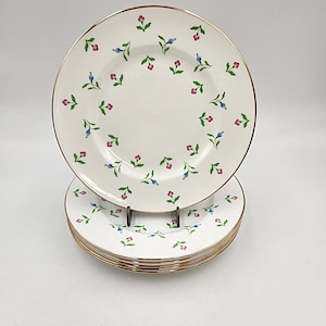 Puede incluir: Un juego de cuatro platos de cena de cerámica blanca con borde dorado y un delicado patrón floral en tonos azules y rosas.