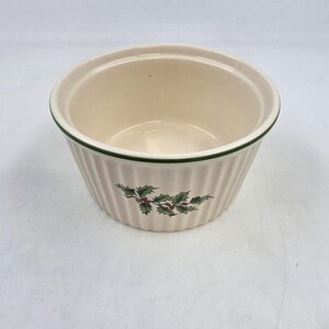 Puede incluir: Un ramequín de cerámica color crema con borde verde y laterales acanalados verticales. Un diseño de acebo y bayas está impreso en el lateral. El ramequín está vacío y listo para usar.