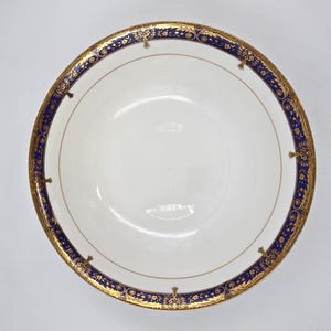 May include: A white porcelain bowl with a decorative blue and gold border. The border features intricate floral and scrollwork designs. The bowl has a simple, elegant design, suitable for serving food or as a decorative piece.