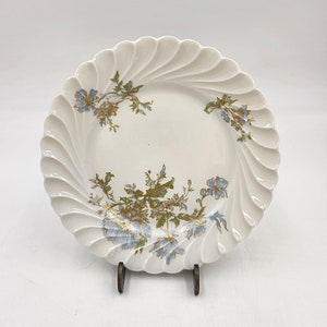 Puede incluir: Un plato de porcelana blanca con un borde festoneado y un diseño floral en tonos azules y dorados.