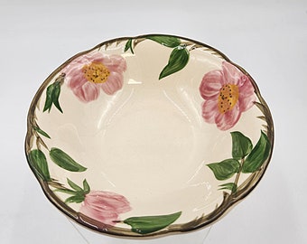 May include: A cream-colored ceramic bowl with a scalloped edge. The bowl is decorated with pink floral designs and green leaves. The rim is brown. The bowl is likely for serving food.