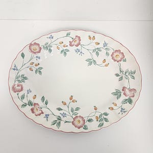Puede incluir: Un plato ovalado blanco para servir con un borde festoneado. El plato está decorado con un patrón floral de rosas rosas y rojas, hojas verdes y bayas amarillas.