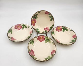 May include: A set of four round ceramic bowls with a cream-colored base and a hand-painted floral pattern featuring pink wild roses, yellow centers, and green leaves. Each bowl has a scalloped edge with a dark brown painted rim detail.