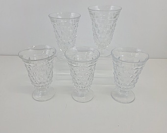 Puede incluir: Un conjunto de cinco copas de vidrio transparente con un patrón de diamantes texturizado en el exterior. Cada copa tiene un borde acampanado, un cuerpo cónico y una base circular de pedestal, dispuestas en formación escalonada.