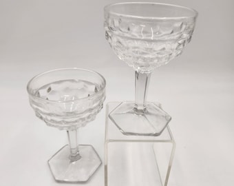 Pode incluir: Duas taças de champanhe transparentes em estilo vintage. As taças apresentam um padrão texturizado em forma de diamante na taça e uma haste com base hexagonal. Uma taça está sobre um suporte de acrílico transparente.