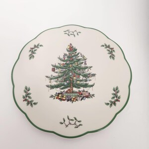 Puede incluir: Un plato de cerámica blanco con un borde festoneado verde presenta un diseño de árbol de Navidad con adornos, regalos y ramas de acebo.