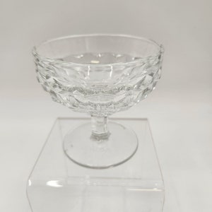 May include: A clear, stemmed glass dessert dish with a diamond pattern around the bowl. The footed base is round and the stem is hexagonal. The glass is transparent, reflecting light.