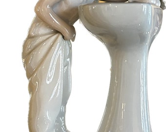 Peut inclure: Une figurine en porcelaine d'une fille lavant un chat dans un évier en porcelaine blanche. La fille porte une chemise et un pantalon blancs. La figurine est sur une base blanche.