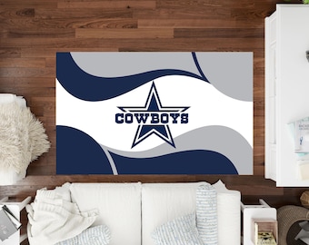 Puede incluir: Alfombra rectangular con el logotipo de los Dallas Cowboys. El diseño incluye una estrella azul marino con la palabra "COWBOYS" en blanco, sobre un fondo blanco con patrones de ondas azul marino y gris. Vista superior.
