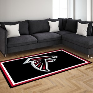 Puede incluir: Una alfombra negra con un borde blanco y un borde interior rojo. La alfombra presenta un logotipo de los Atlanta Falcons en plata y rojo en el centro.